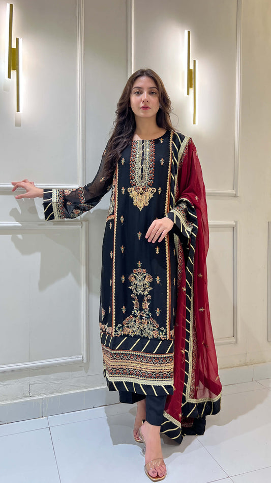 Woman wearing black chiffon embroidered shalwar kameez with maroon dupatta, standing in traditional pose